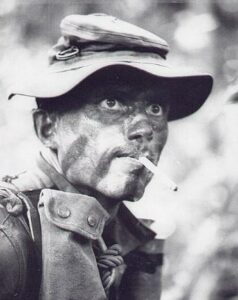 AP Wire Photo 1968 A unidentified Recon Marine with face paint and bush hat decorated with grenade pins rest after a sweep near the U.S. Marine base at Kha Sahn.